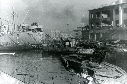 Heavily damaged port of Naples with U.S. Liberty ship and two smaller vessels docked beside burned out building.  Part of the research collection of the U.S. Army Transportation Museum.