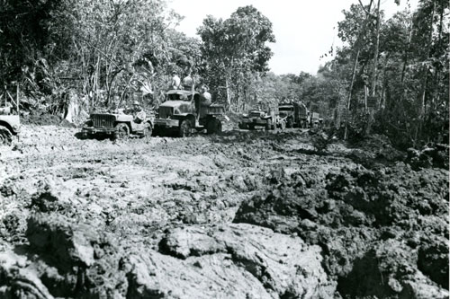A U.S. Army truck convoy makes it way on muddy roads to ration dump in New Georgia Islands during World War II in the Pacific.  Part of the research collection of the U.S. Army Transportation Museum.
