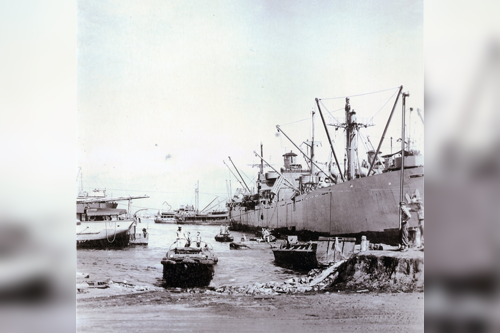 Crowded harbor in Lae, New Guinea with various cargo ships and DUKWs coming to shore in 1944.