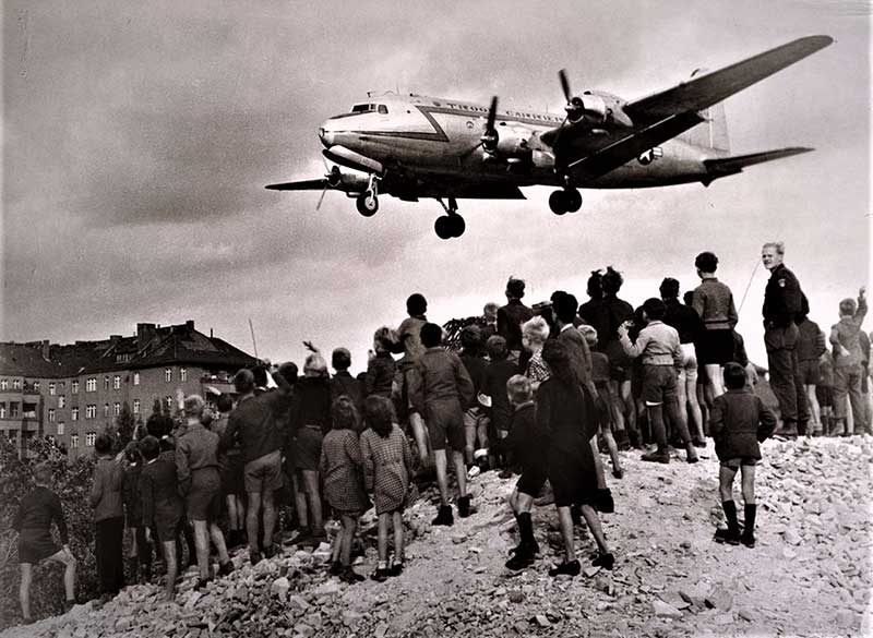 Low flying plane passing over a large group of people gathered on a hill.