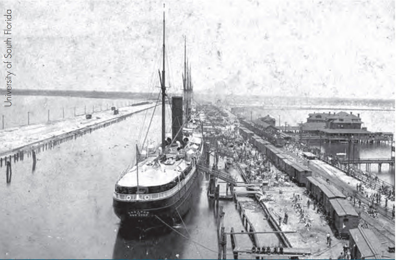 View of a dock at the port of Tampa with moored ships and boxcars being unloaded, c. 1898