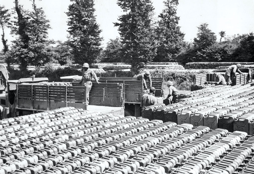 Trucks from different units draw cans of gasoline 7 February 1945 from one of the storage fields in the quartermaster depot. After the five-gallon “jerricans” were washed, they were refilled from tankers on the beachheads and returned to the quartermaster depot. (Photo courtesy of the U.S. Army)