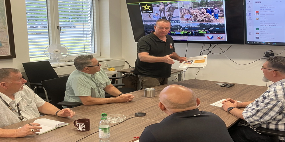 Courtesy Photo | John Schulz (center) briefs some of his fellow staff members from Army Field Support Battalion-Germany at the battalion conference room in Vilseck, Germany, July 18, 2025. Schulz is a transportation specialist at AFSBn-Germany in support operations. He’s also a State of California National Guardsman and a lieutenant colonel who, in addition to this, served for 20 years in the active Army and 16 years in the U.S. Army Reserve. (U.S. Army courtesy photo).